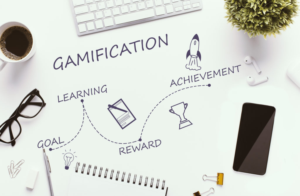 Gamification stages on white workplace - goal, learning, reward and achievement, top view