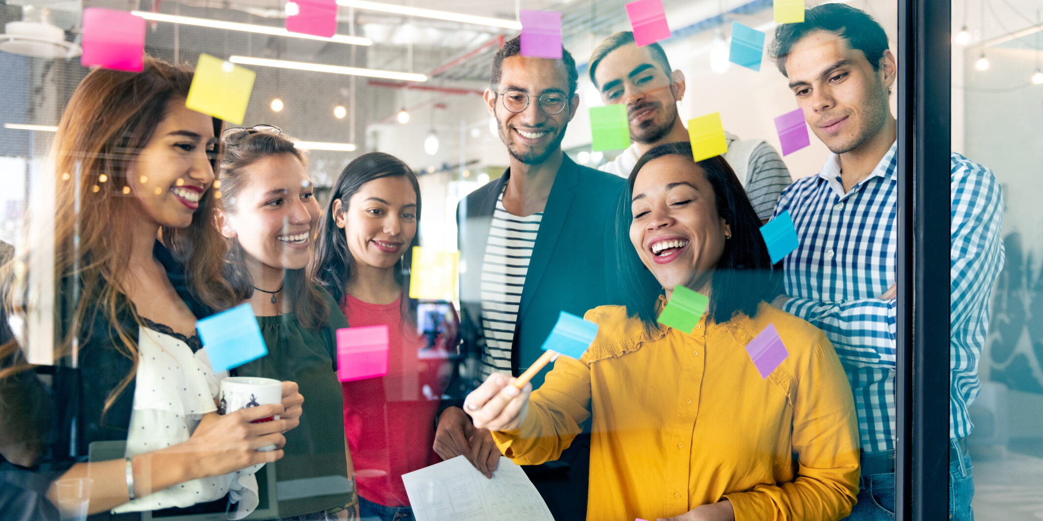 Young professionals planning tasks on glass wall with adhesive notes in co-working office